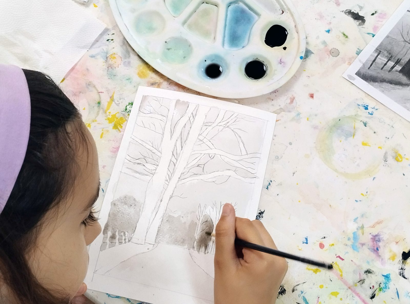 Niña pintando un paisaje de árboles en acuarela en una clase de pintura para niños en Sevilla Este
